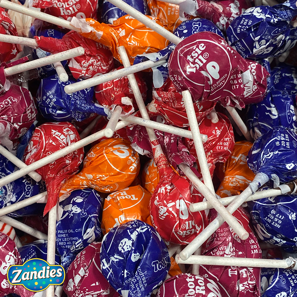 large pile of individually wrapped tootsie roll lollipops, red, blue orange, brown, and individually wrapped. Zandies logo in the corner.